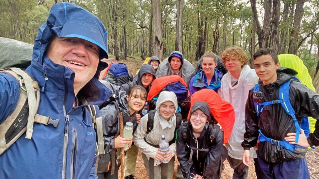 Didier and a group of teen hikers smiling in the rain