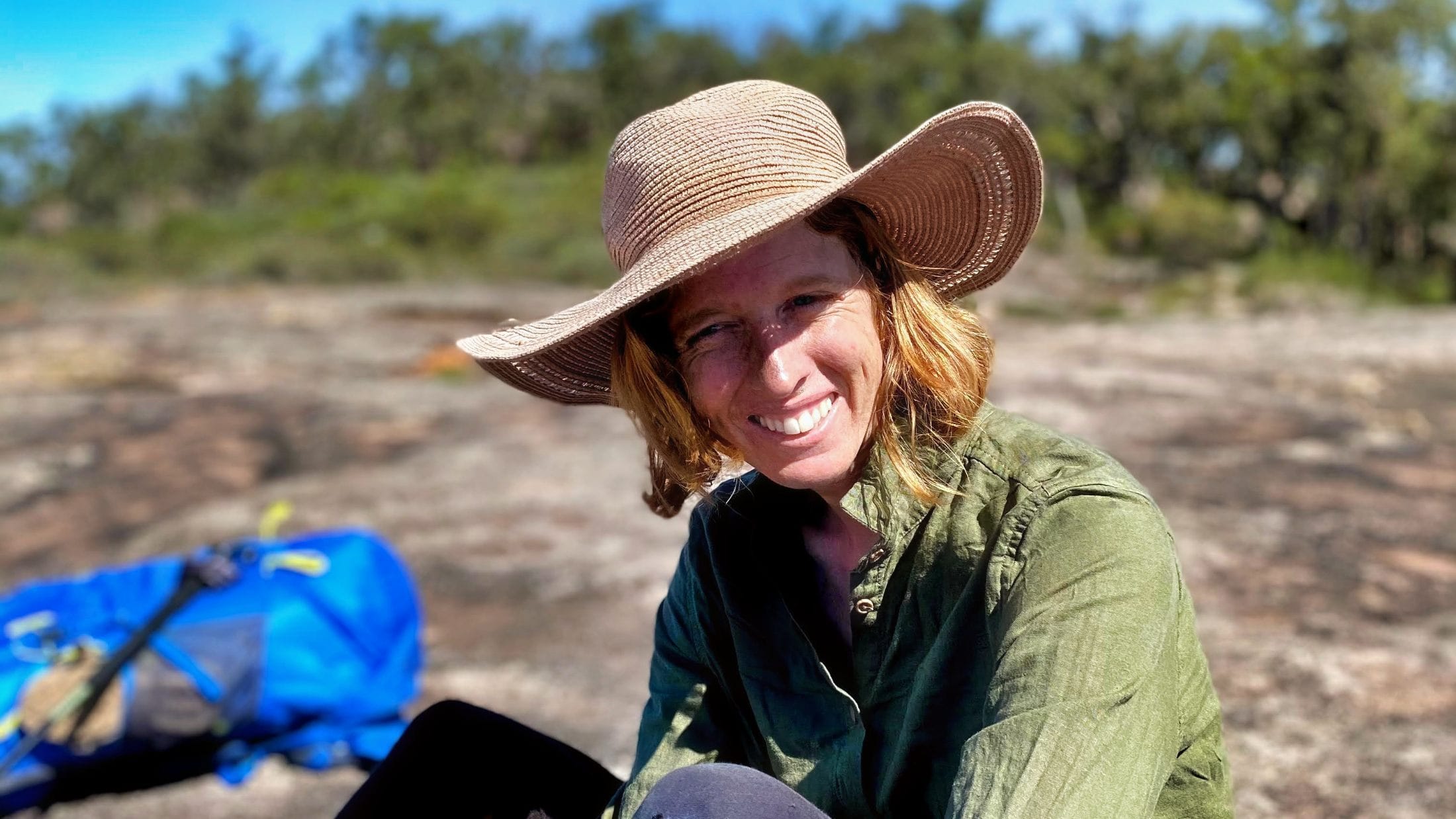 Smiling hiker in a broad-brimmed hat resting on a granite outcrop